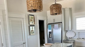 A kitchen with a marble countertop, blue cabinets, a stainless steel refrigerator, and two wicker pendant lights.
