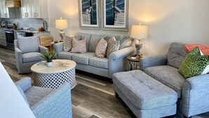 A modern living room with grey sofas, a round coffee table, and a dining area with a kitchen in the background.