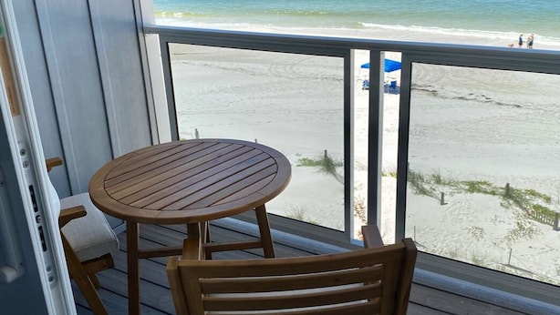 A wooden deck with a round table and chairs, overlooking a beach with a clear view of the ocean and a distant shoreline.