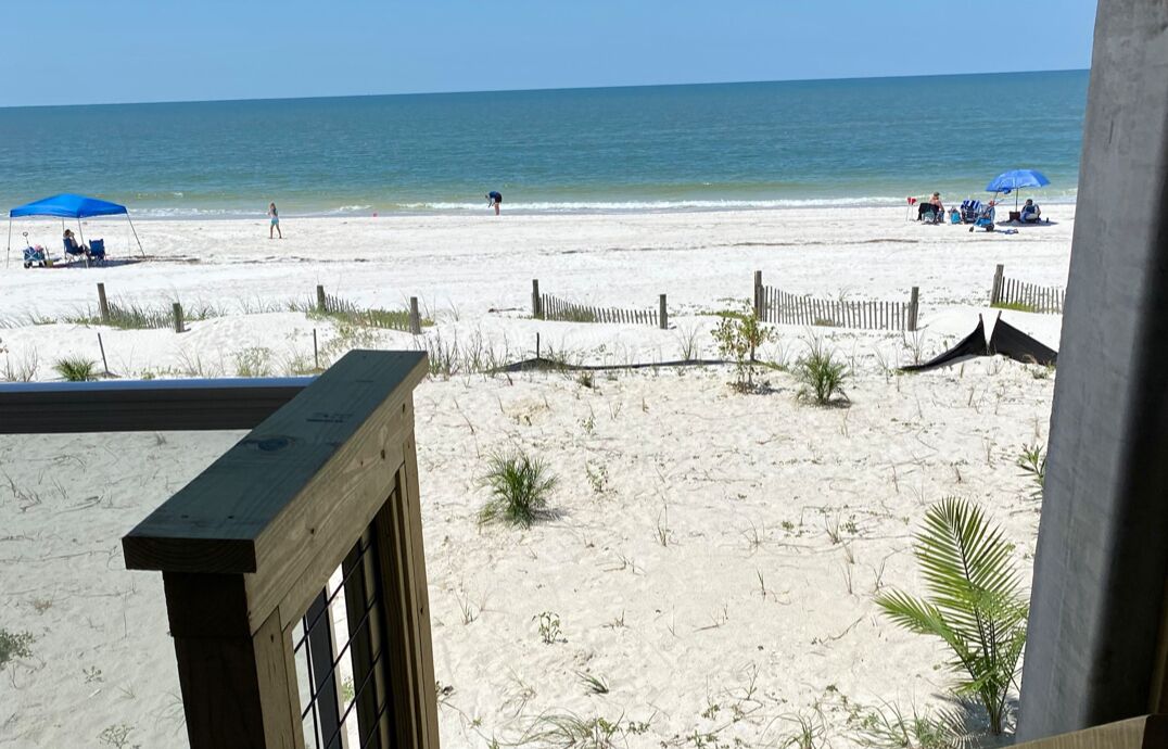 Une vue sur la plage depuis un balcon doté d’une balustrade en bois, avec une plage de sable et une clôture en bois.