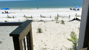 A beach view from a balcony with a wooden railing, a sandy beach, and a wooden fence.