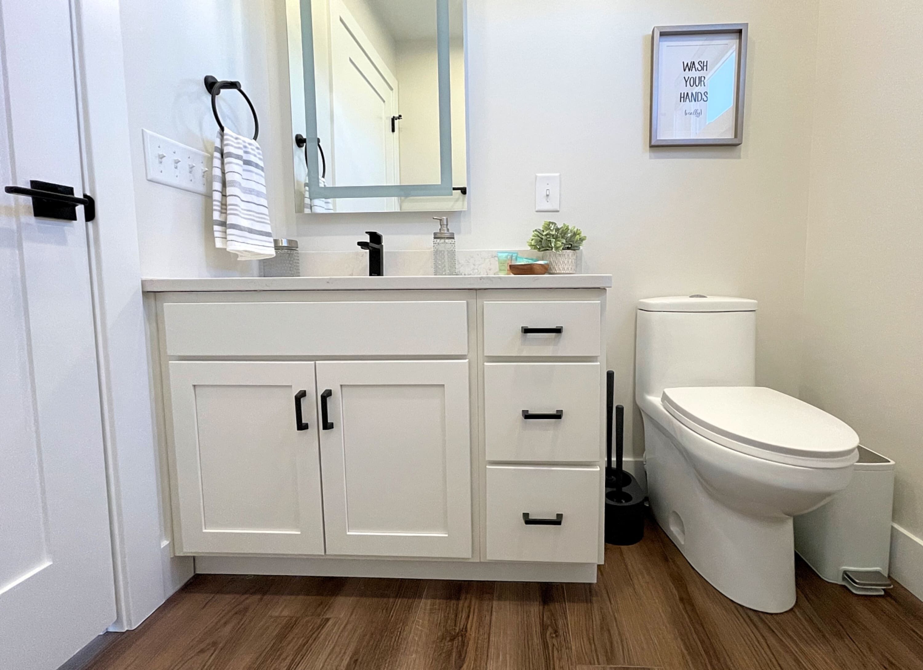A bathroom with a white vanity, a toilet, and a framed quote on the wall.