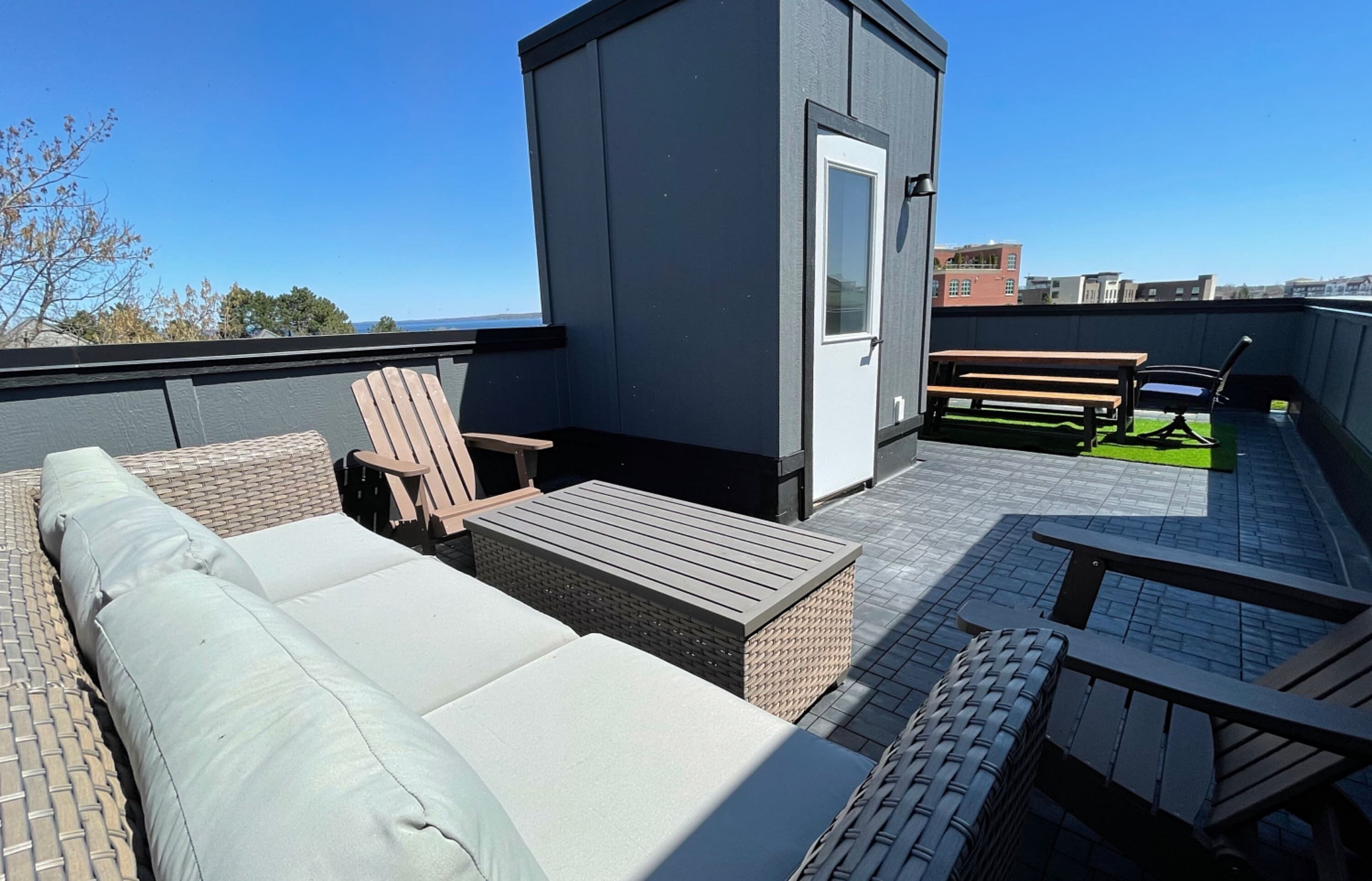 Eine Dachterrasse mit einer Couch, Stühlen, einem kleinen Tisch und einer Tür.
