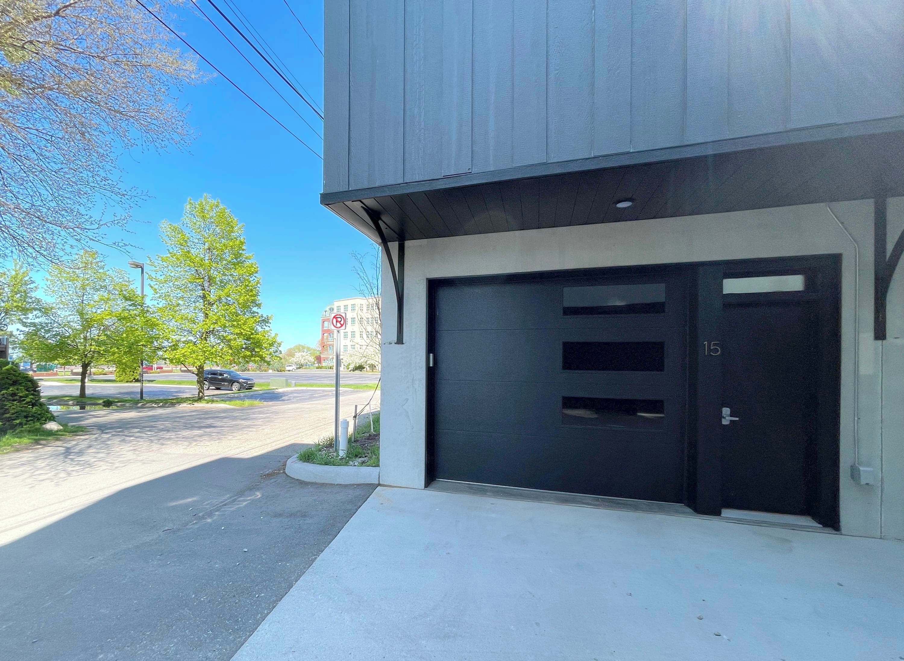 A building with a garage door, a sidewalk, and a street with cars and trees.