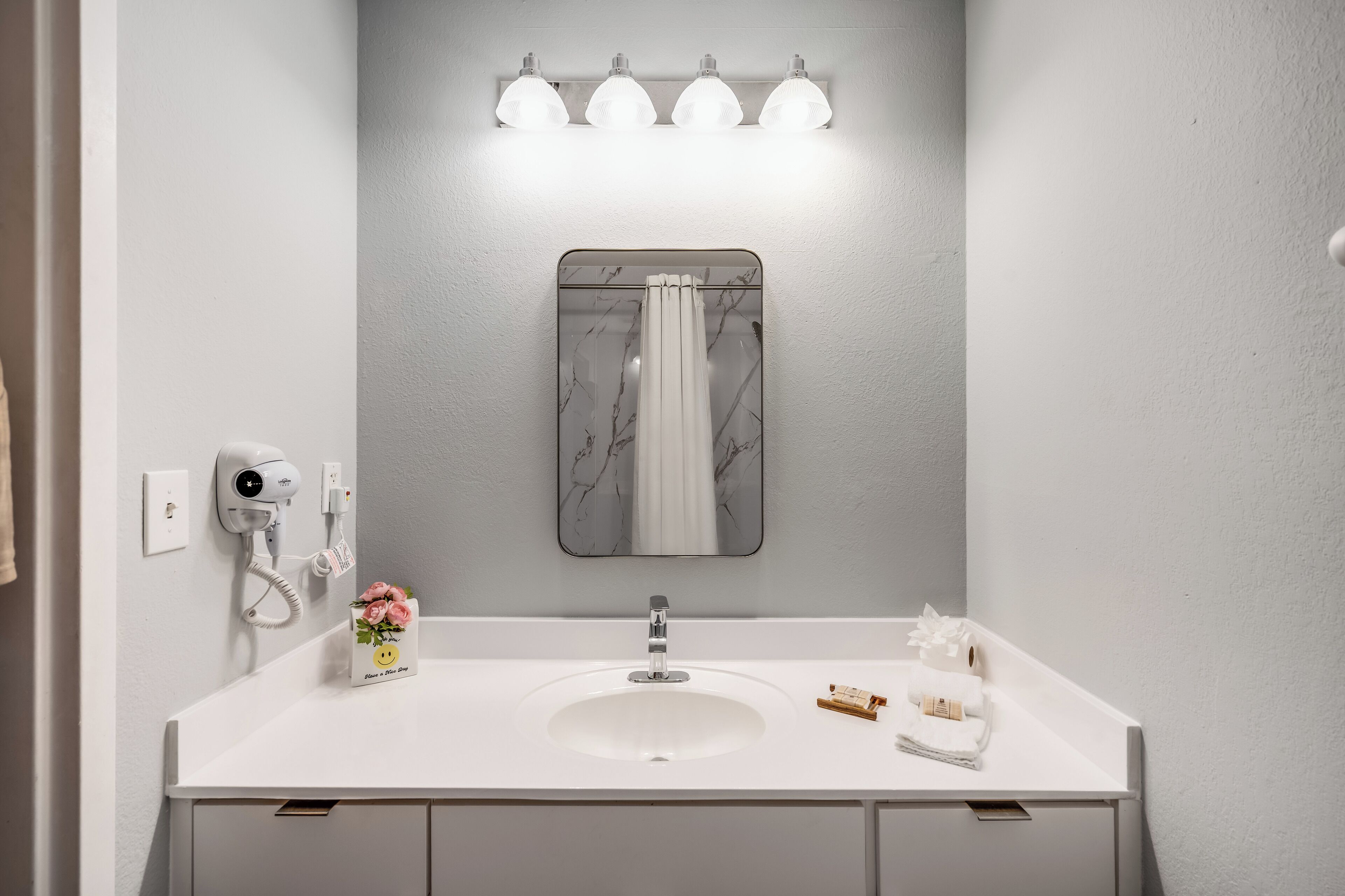 A modern bathroom with a white sink, a mirror, and a hairdryer on the wall.