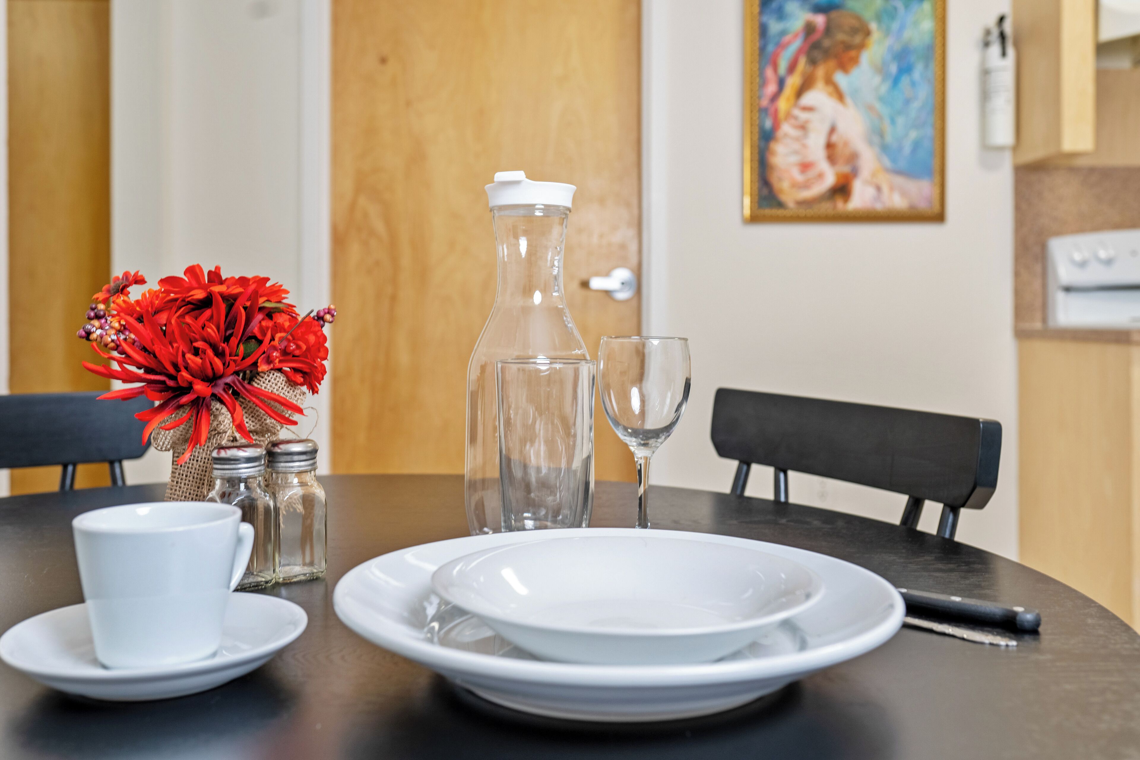 A dining table set with plates, a glass pitcher, salt and pepper shakers, a white cup, and a wine glass.