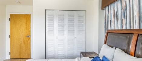 A bedroom with a bed, a wooden door, a closet with white louvered doors, and a headboard with a wooden frame.