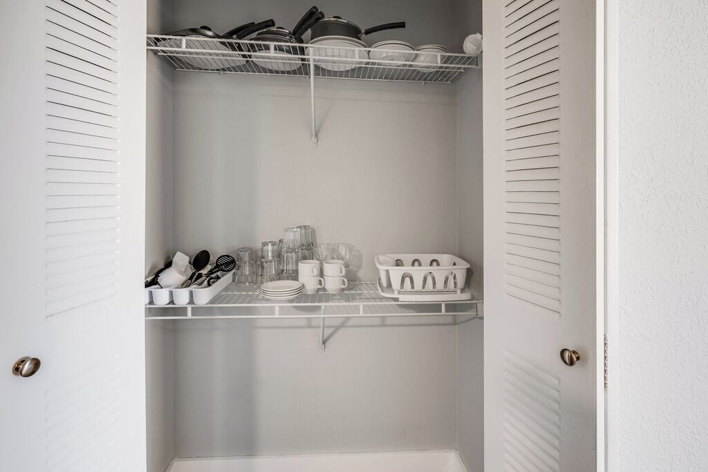 Una dispensa in cucina con scaffali che contengono pentole, stoviglie e bicchieri.