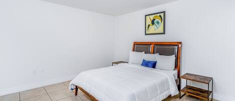 A bedroom with a bed, nightstands, a painting, and tiled flooring.