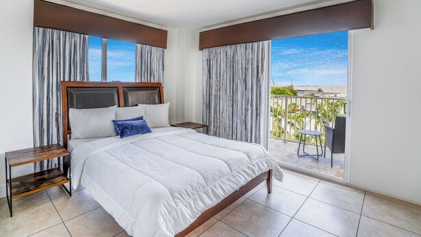 A hotel room with a large bed, two nightstands, a view of the outdoors, and a balcony with a table and chairs. - South River Suites (Miami)