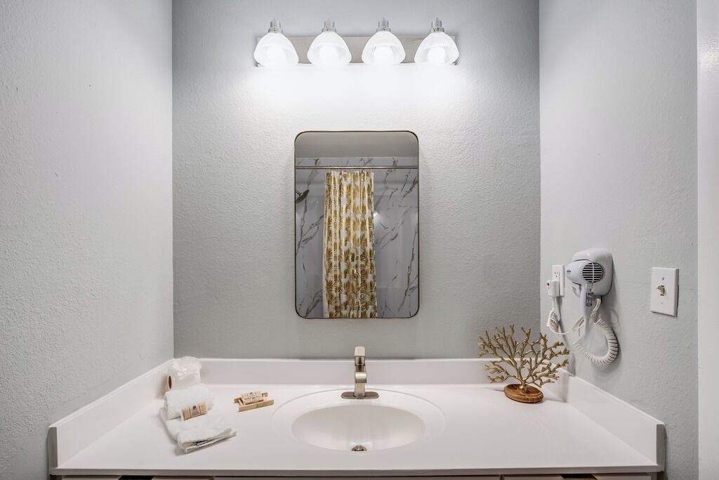 A bathroom with a white sink, a mirror with a marble-like frame, and a hairdryer mounted on the wall.