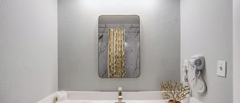 A bathroom with a white sink, a mirror with a marble-like frame, and a hairdryer mounted on the wall.