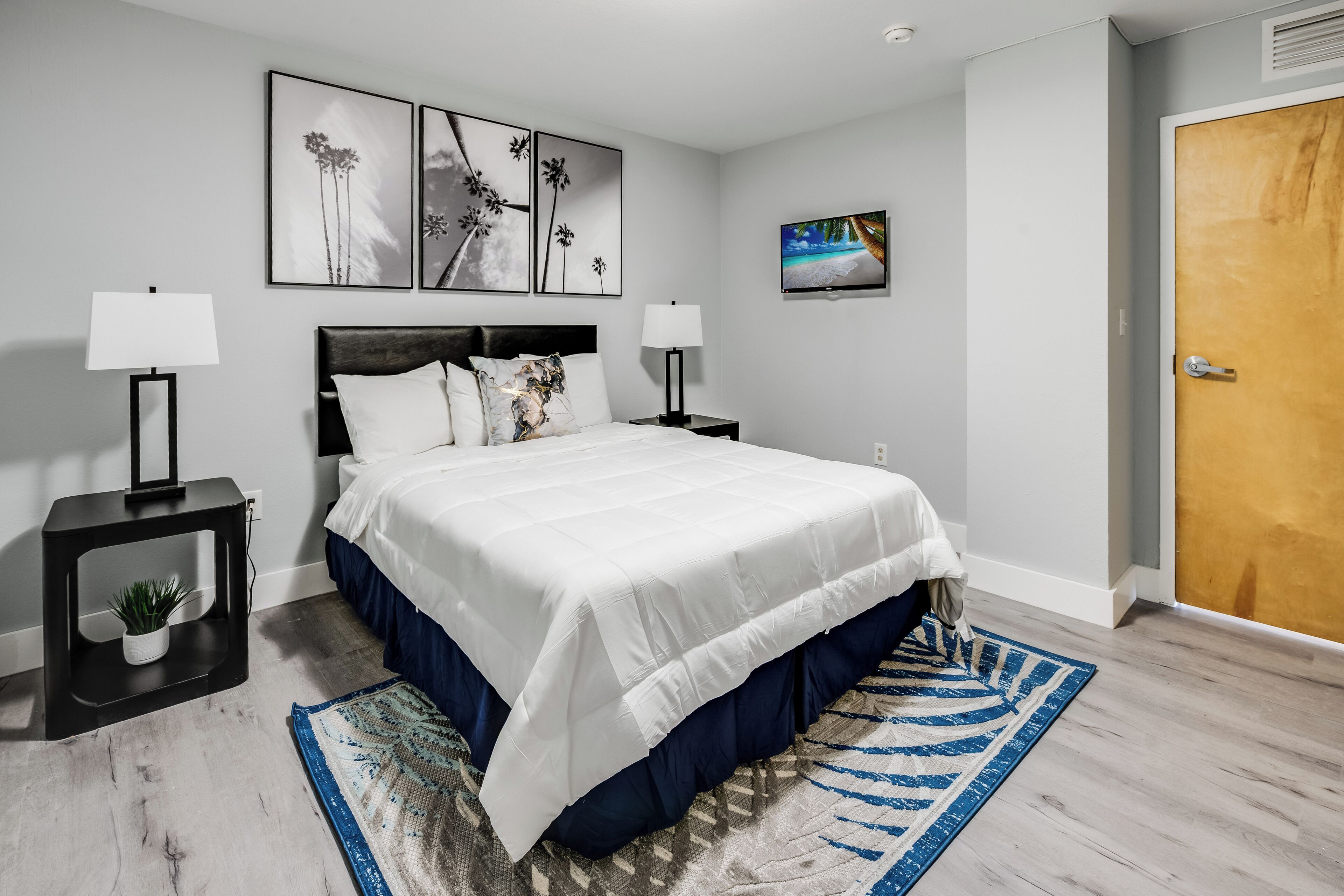 A neatly arranged bedroom with a large bed, two bedside tables with lamps, a flat-screen TV, and a door.