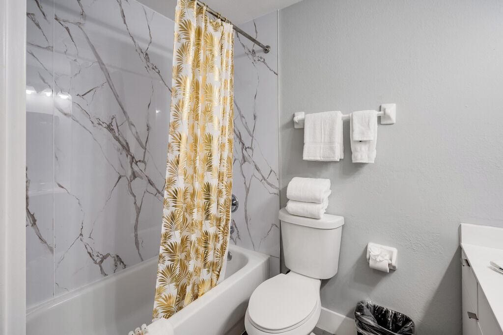 Un baño con bañera, inodoro y cortina de ducha con estampado de hojas.