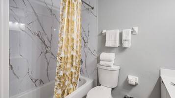 Un baño con bañera, inodoro y cortina de ducha con estampado de hojas.