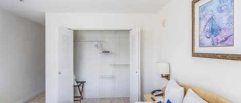 A hotel room with a bed, a nightstand, a lamp, a framed artwork, and a closet with shelves.