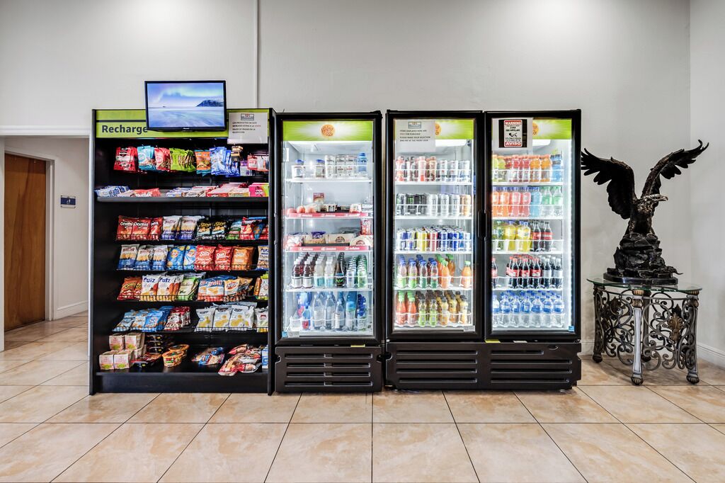 A row of beverage dispensers with snacks and a television screen above them.