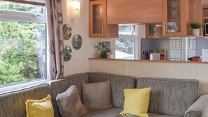 A cozy living area with a sofa, cushions, a kitchen area with cabinets and appliances, and a window with curtains. - A perfect countryside escape for lovers of the outdoors. (Ayr)