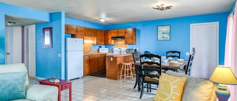 A compact living space with a kitchenette, a dining area, and a seating area with a lamp and cushions.