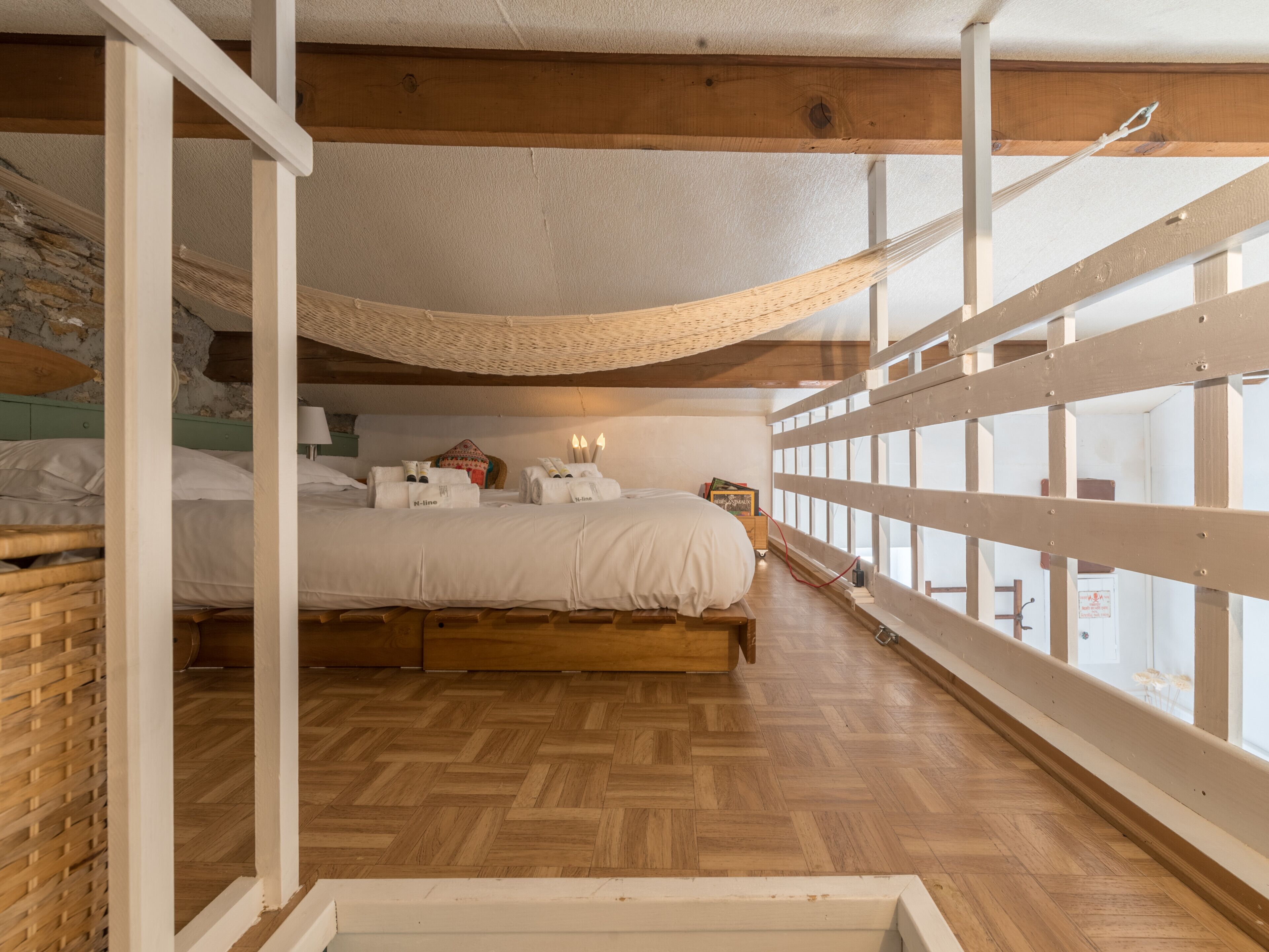 Un dormitorio con cama de madera, suelo con diseño de espiga y vista por una ventana con barandilla de madera.