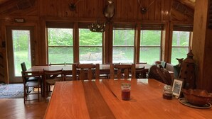 A wooden dining area with a large table, chairs, and a view of the outdoors through large windows.