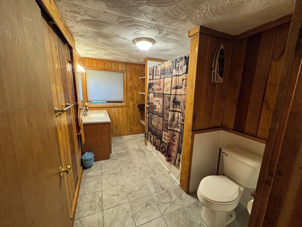 Une salle de bain avec des murs en bois, un lavabo, des toilettes et un espace douche.