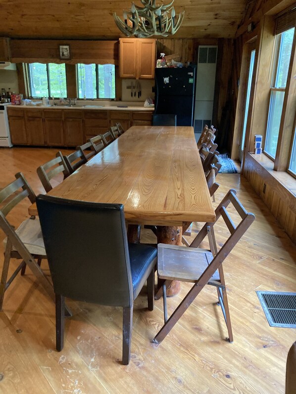 Un gran comedor de madera con sillas, una zona de cocina con armarios de madera y un amplio ventanal con persianas.