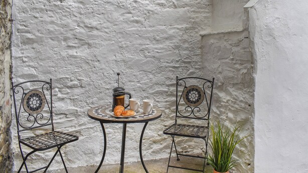 A small outdoor seating area with two metal chairs and a round table, a coffee pot, and a croissant. - 3 bedroom accommodation in Bala (Bala)