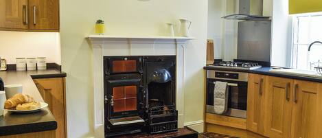 A kitchen with a fireplace, wooden cabinets, a clock, and a tiled floor.