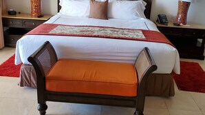 Une chambre d’hôtel avec un grand lit, une tête de lit en bois, deux tables de chevet avec des lampes, un tapis rouge et un banc au pied du lit.