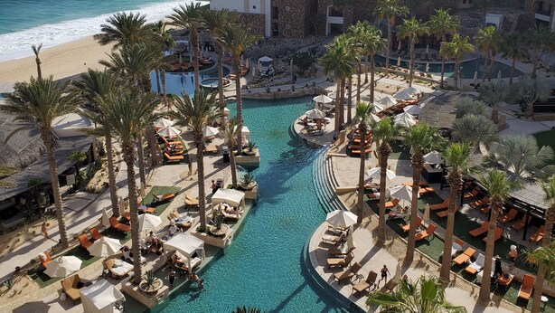 Un complexe hôtelier doté d’une piscine centrale, de palmiers et offrant une vue sur la plage.