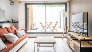 A modern living room with a sofa, a coffee table, a TV, and a dining area with chairs.