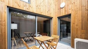 A wooden exterior with a sliding glass door leading to an outdoor seating area with a table and chairs.