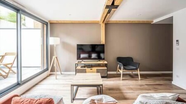 A modern living room with a large window, a flat-screen TV, a wooden ceiling, and a minimalist design.