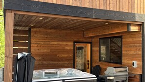 Una cabaña de madera con jacuzzi, parrilla y zona de estar exterior cubierta.
