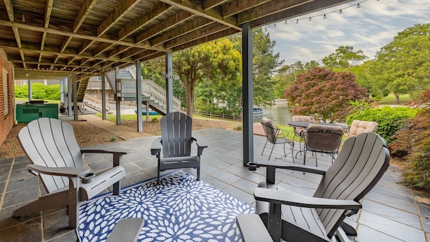 En udendørs terrasse med Adirondack-stole, et mønstret tæppe og udsigt til en have og en bygning i baggrunden.
