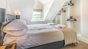 Une chambre à coucher comprenant un lit, une table de chevet, une fenêtre, une bibliothèque intégrée et un luminaire suspendu.
