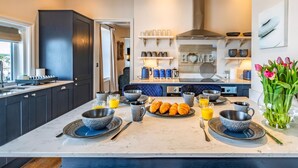 Une cuisine moderne avec des meubles de couleur sombre, un plan de travail en marbre et un îlot central où sont disposés des aliments pour le petit-déjeuner.