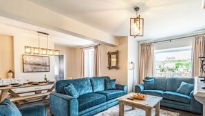 Un salon spacieux avec deux canapés bleus, une table basse en bois et un coin repas comprenant une longue table et des chaises.