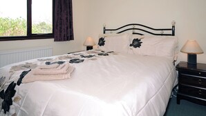 Una cama bien hecha con ropa de cama floral, dos lámparas de noche y una ventana con cortinas.