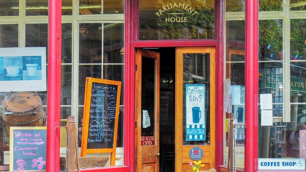 Una cafetería con fachada roja, puerta de madera y cartelera con el menú.