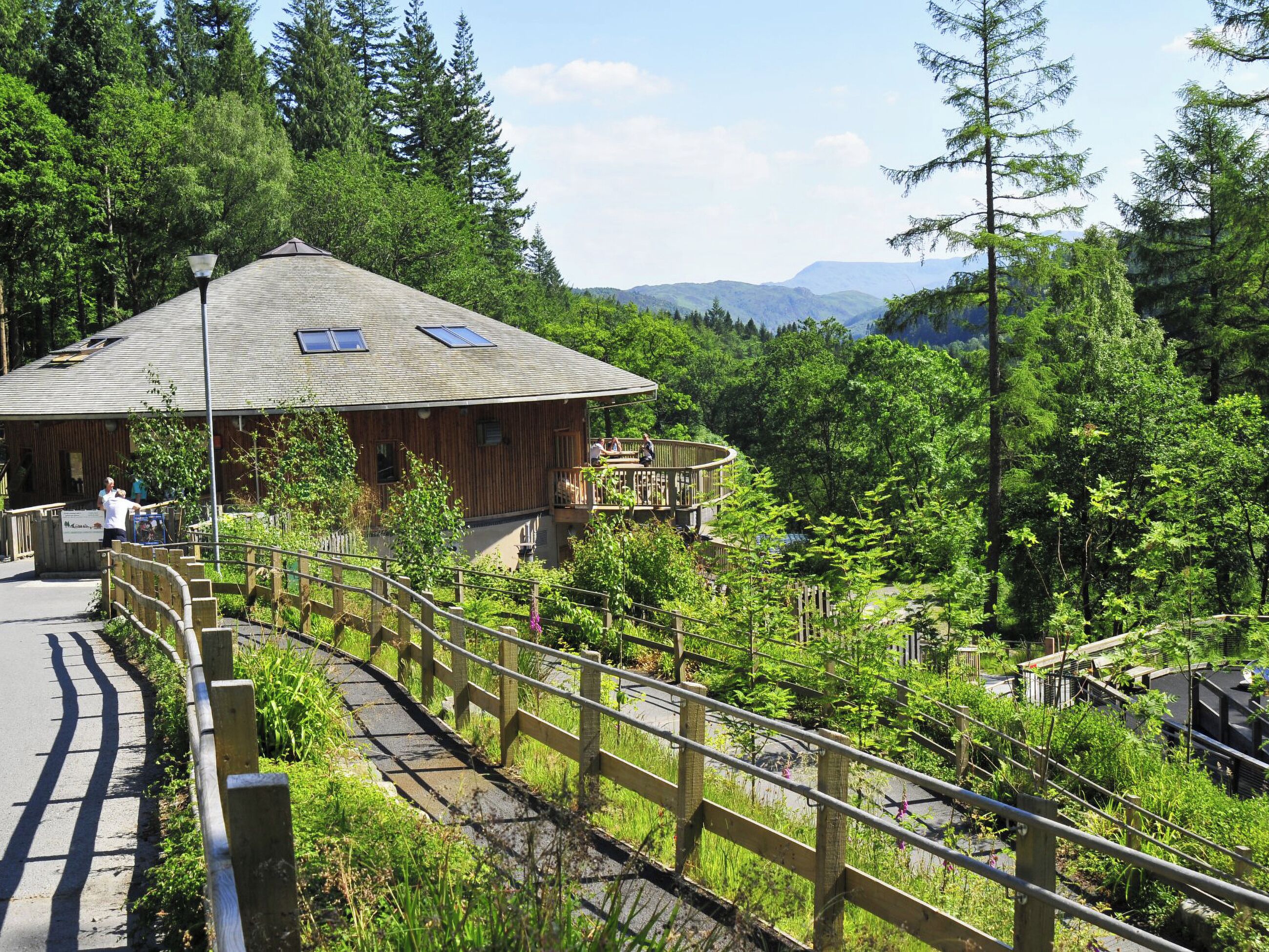Een houten chalet met balkon, omringd door weelderige begroeiing en bergen op de achtergrond.