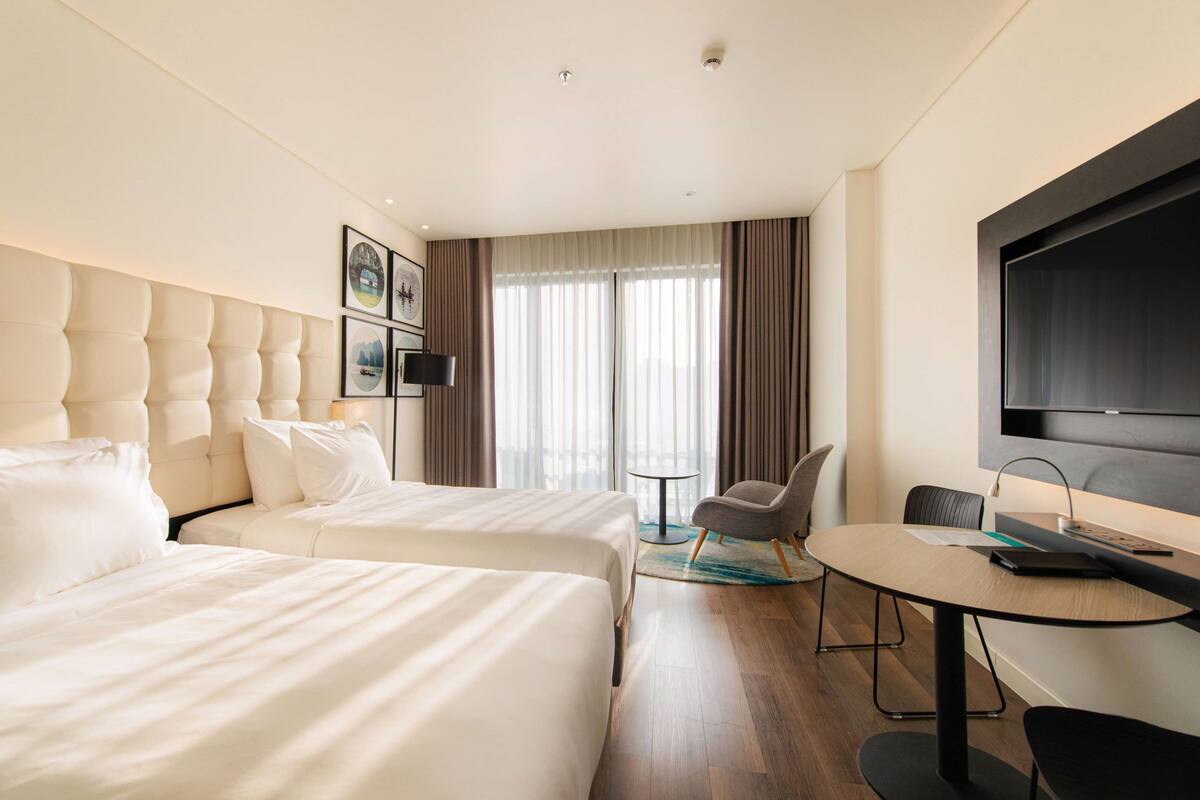 A hotel room with two beds, a TV, a small table, and a chair.