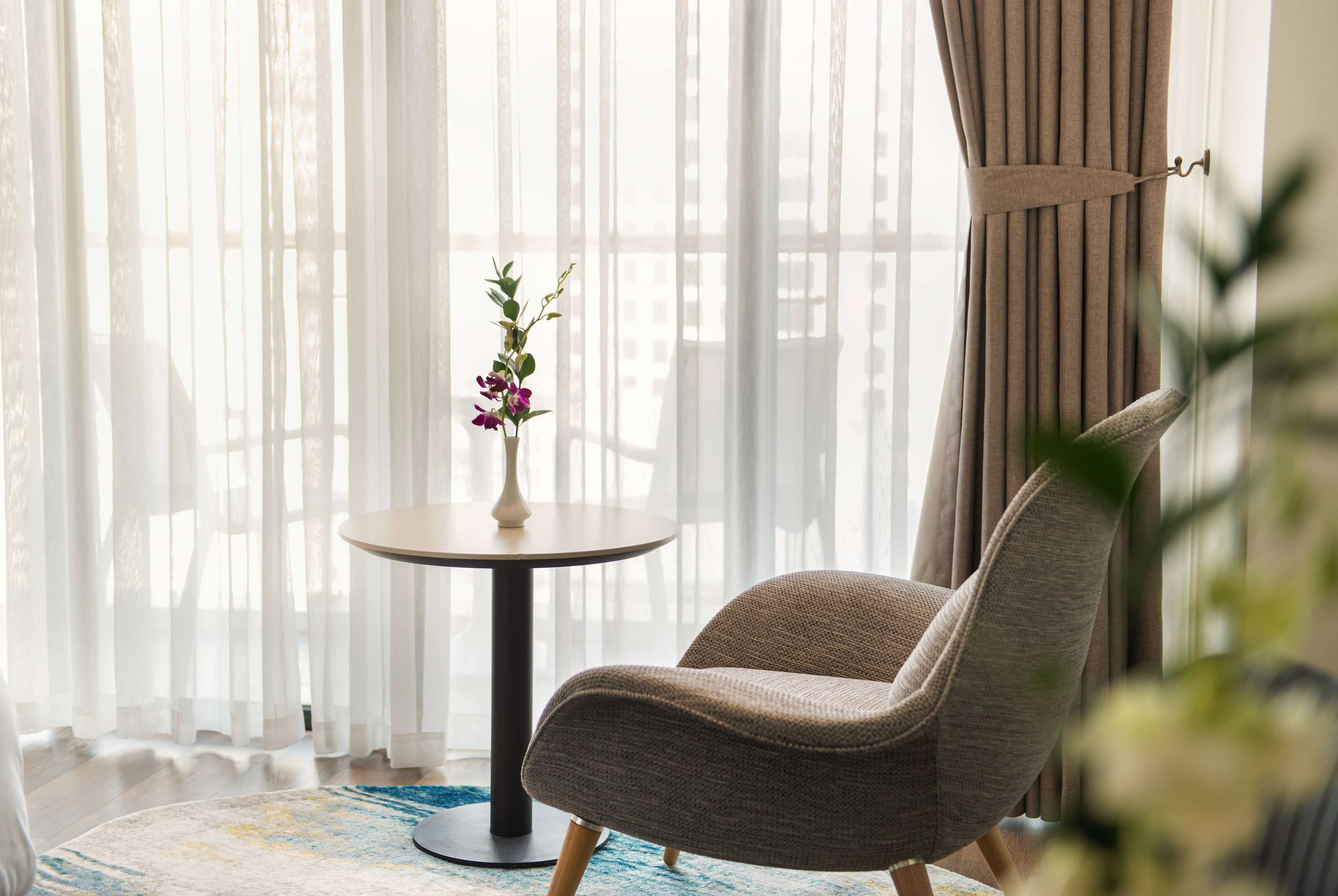 A room with a round table, a chair, and a vase with flowers.