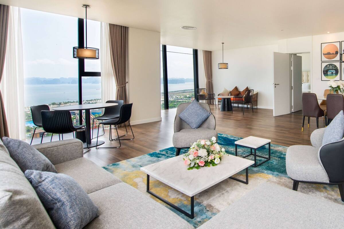 A modern living room with a large window, a dining area, and a view of the sea.