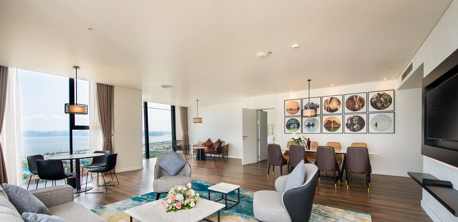 A modern living room with a dining area, large windows, and a view of the sea.