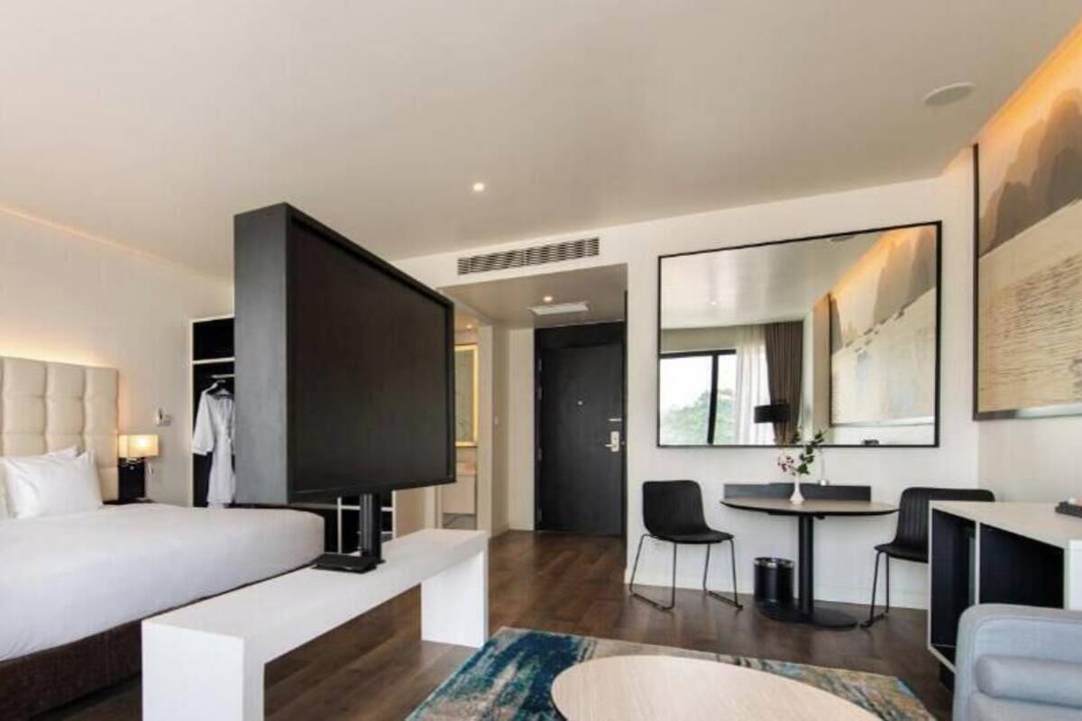 A modern hotel room with a large bed, a TV, a desk, and a chair.