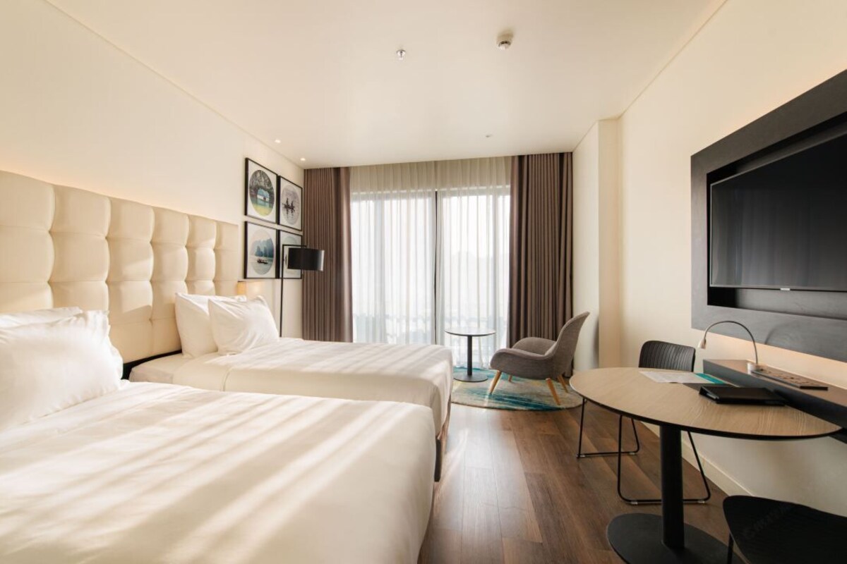 A hotel room with two beds, a desk, a chair, a TV, and a window with curtains.