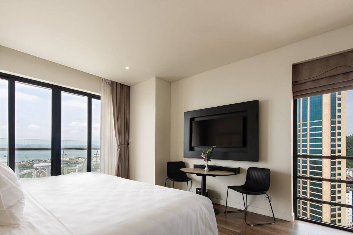 A hotel room with a large bed, a TV mounted on the wall, a balcony with a view, and a small table with two chairs.