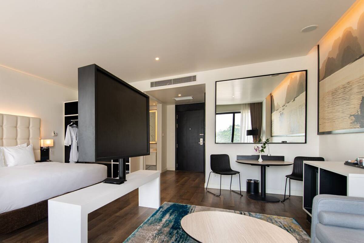 A modern hotel room with a large bed, a flat-screen TV, a desk, and a chair.